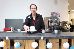 Eine Frau bietet einem über den Tresen hinweg eine Tasse Kaffee an