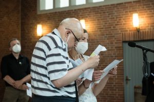 Ein Mann und eine Frau stehen an einem Mikrofon und verlesen einen Gebetstext bei der Einführung von Pastorin Anja Vollendorf