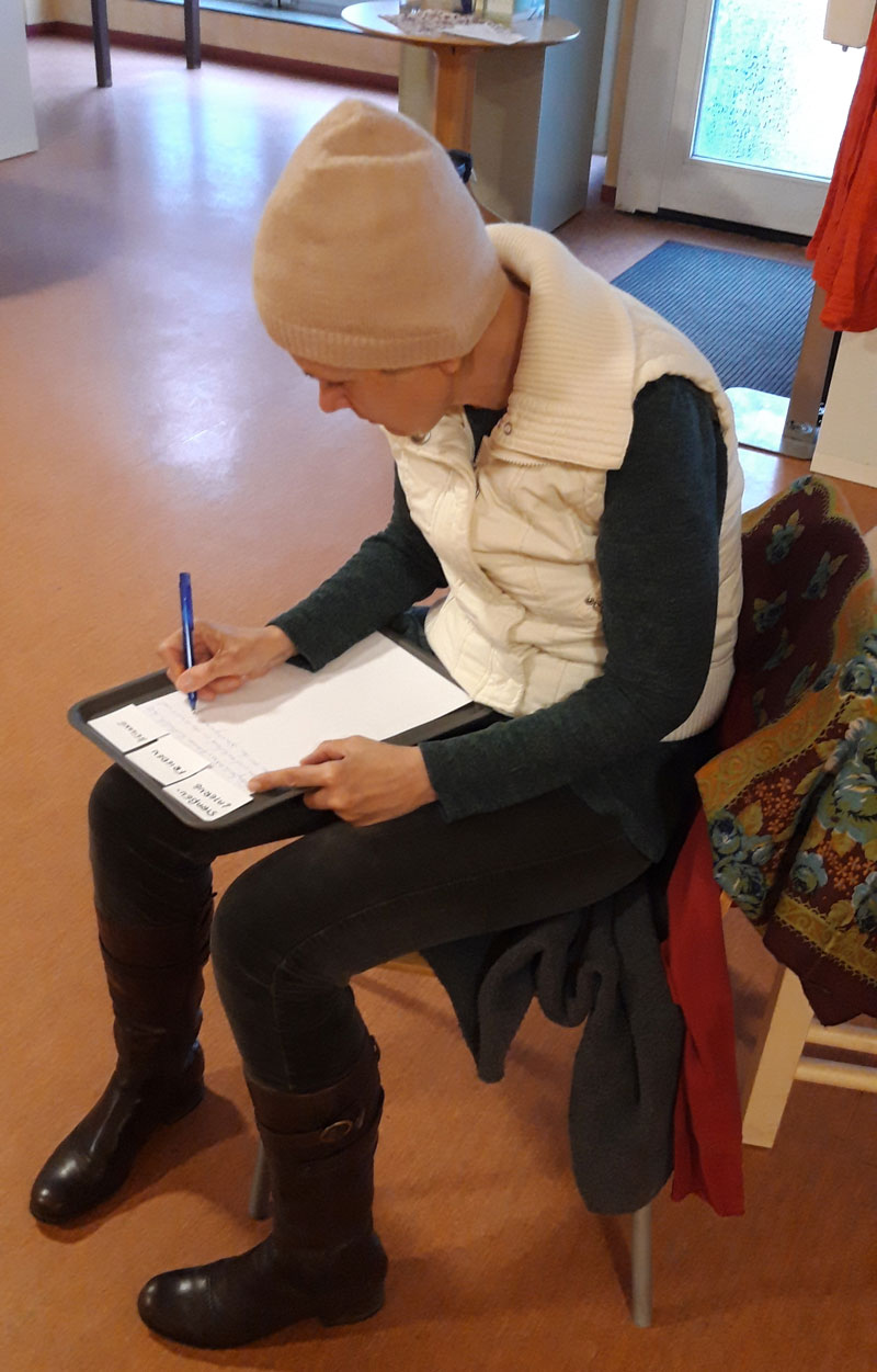 Eine Teilnehmerin der Schreibwerkstatt im frauenzimmer Ein Frau mit Mütze sitzt auf einem Stuhl und schreibt
