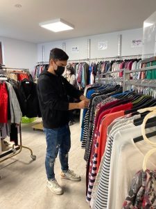Ein junger Mann hängt Bekleidung an Kleiderständer.