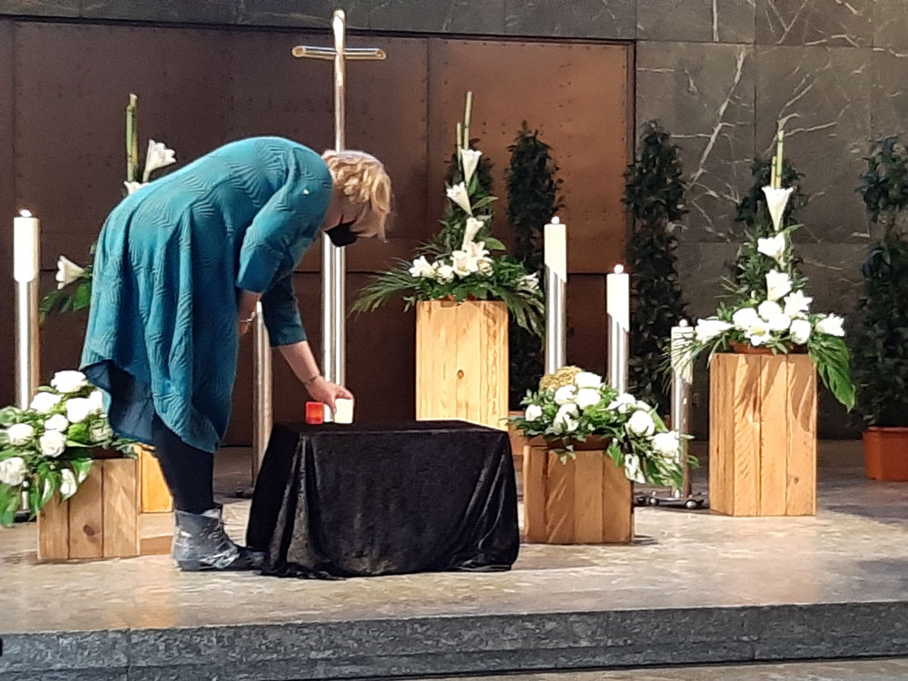 Eine Frau in blauem Kleid zündet in einer Kapelle KErzen an.