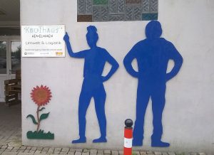 Zwei große Pappmenschen in blauer Farbe sind auf einer Hauswand angebracht