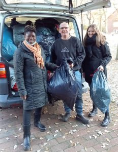 Zwei Frauen und ein Mann stehen vor einem Pkw mit Kleiderspenden.