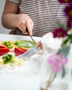 Eine Frau schneidet Paprika ist Würfel. Vor ihr steht eine Vase