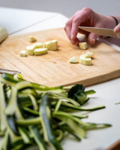 Eine Person schneidet Zucchini in kleine Würfel. Zu sehen ist die Hand mit dem Messer und die Würfel