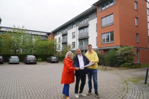 Drei Menschen stehen vor einem GEbäude und halten einen Plan in der Hand.