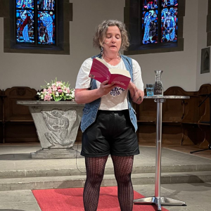 Eine Frau steht vor einem Mikrofon und liest aus einem Buch vor