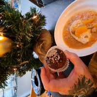 Hand mit einem Muffin und ein Teller Nachtisch, alles sehr weihnachtlich
