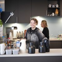 Zwei Frauen, die hinter einem Küchentresen stehen. Eine der Frauen lächelt in die Kamera