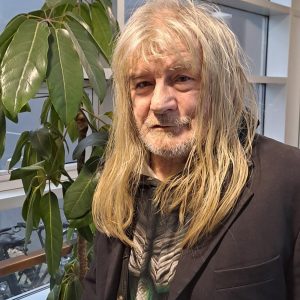 Ein Mann mit langen blonden Haaren und einem schwarzen Jacket